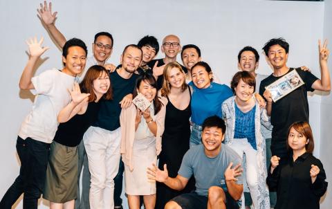 Tessa stands at the centre of a large group of her smiling CRAZY Inc. colleagues