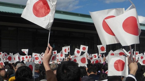 A crowd of people hold and wave small Japanese flags