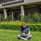 Student using laptop on the grass in front of the faculty building