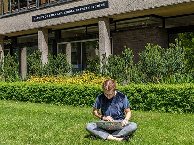 Student using laptop on the grass in front of the faculty building