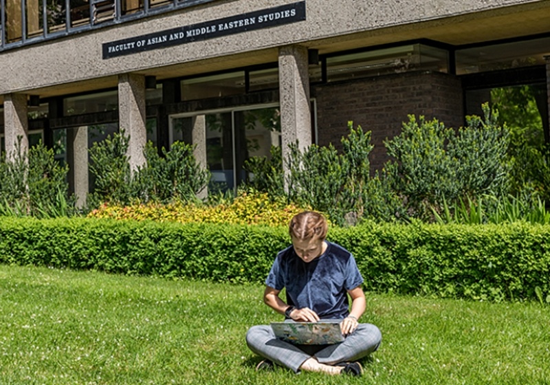 Student using laptop on the grass in front of the faculty building